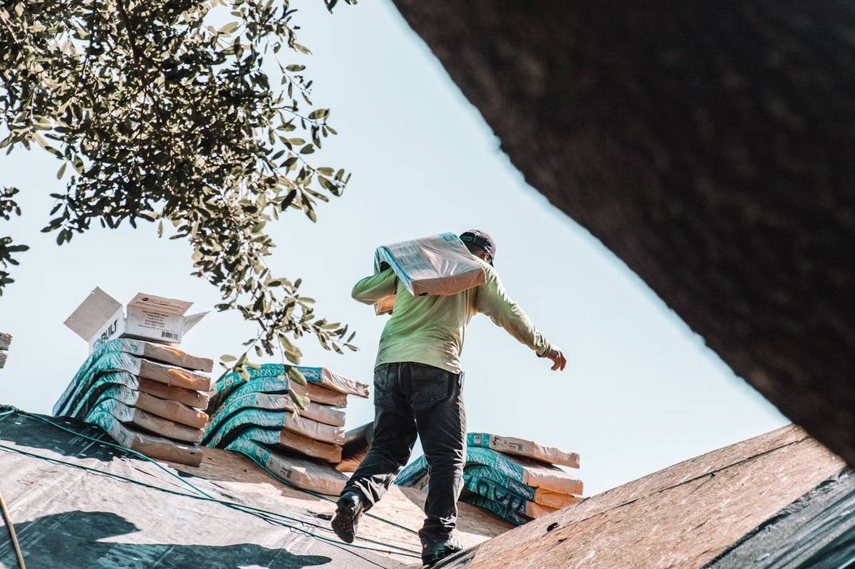 A roofer carrying a bundle of shingles across a roof