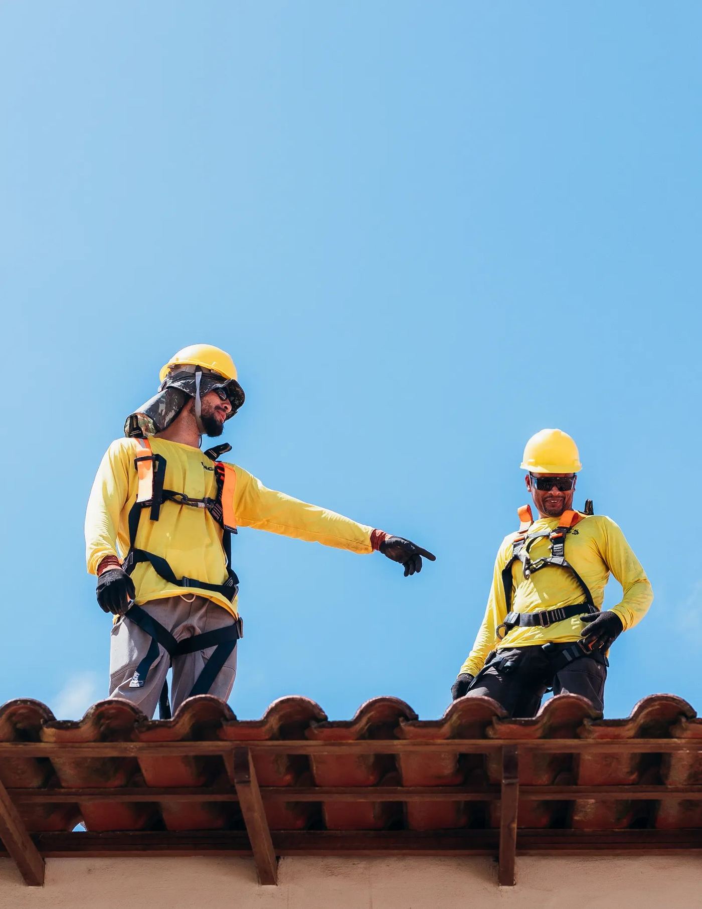 Two roofers in safety gear working on a tile roof